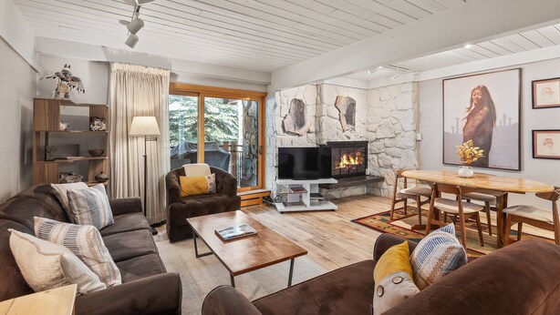 A cozy living room with a stone fireplace, wooden furniture, and a large window. - 715 Stonebridge Condos Slopeside Western Decor Full Kitchen (Snowmass Village)