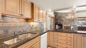 Une cuisine dotée de plans de travail en granit, de meubles en bois, d’un lave-vaisselle encastré et d’un mur décoratif en pierre.