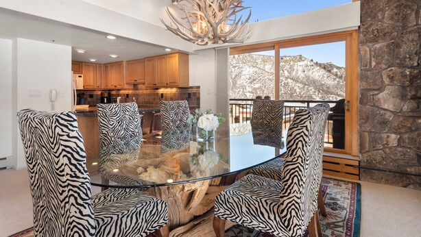 Un espace repas avec une table en verre entourée de chaises à motifs zébrés, un plafond en bois et une vue sur une montagne enneigée.