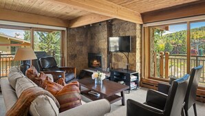 Un salon chaleureux avec une cheminée en pierre, des fauteuils confortables et une grande fenêtre donnant sur un paysage magnifique.