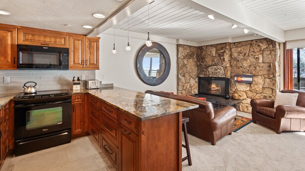A kitchen with wooden cabinets, a black microwave, and an oven. There's a stone wall with a fireplace and a round mirror.