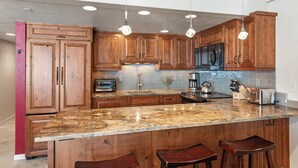 A kitchen with wooden cabinets, a granite countertop, and hanging pendant lights.