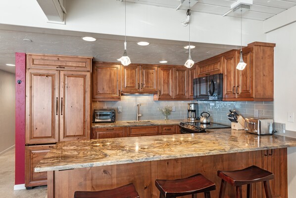 A kitchen with wooden cabinets, a granite countertop, and hanging pendant lights.