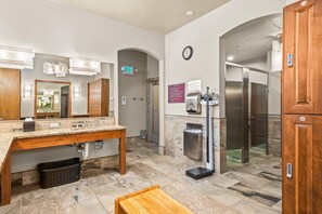 A modern bathroom with a marble countertop, a sink, a mirror, a clock, and a shower area.