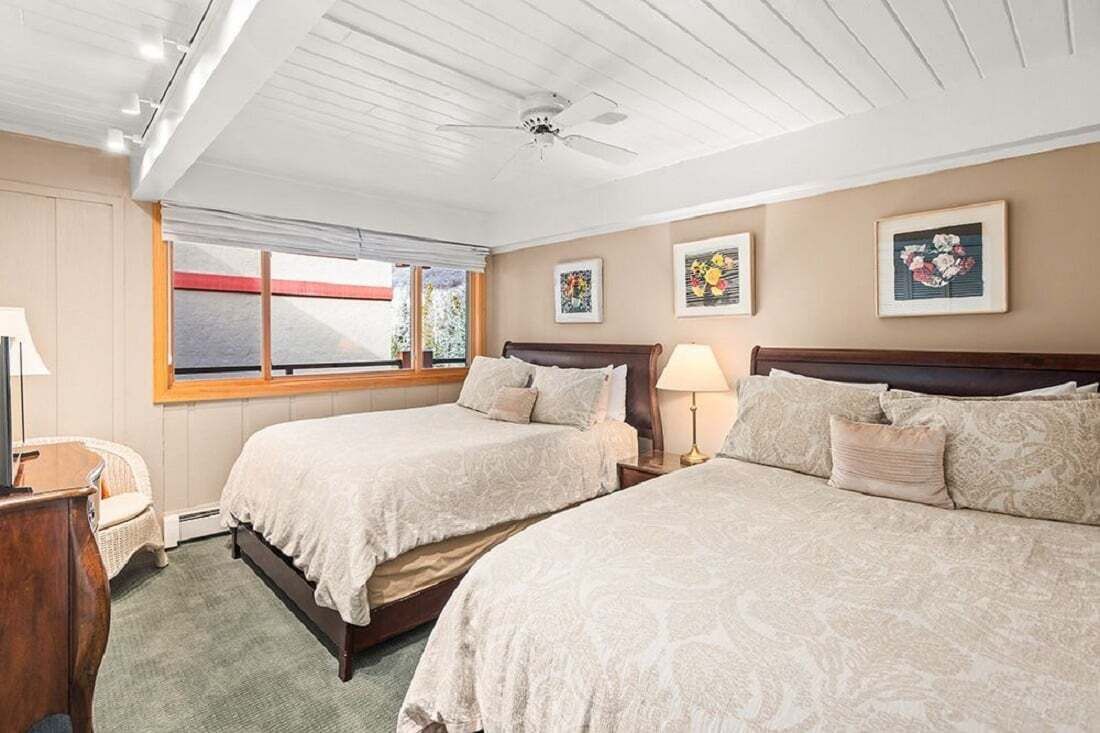 Une chambre avec deux lits, un ventilateur de plafond, une fenêtre avec vue et des œuvres d’art encadrées accrochées au mur.