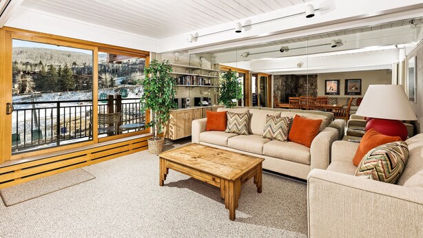 A spacious living room with a large window, a wooden coffee table, a beige sofa with colorful cushions, and a red floor lamp. - Ski-in/Ski-out Stonebridge Condo 922, Pool & Hot Tubs (Snowmass Village)