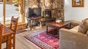 Un salon chaleureux avec une cheminée en pierre, des meubles en bois et un grand téléviseur posé sur un meuble en bois.