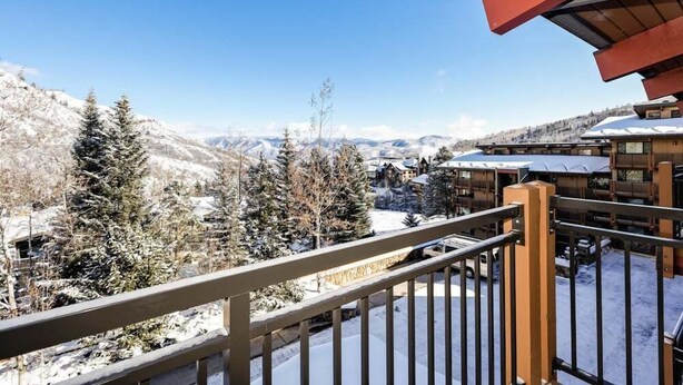 Un paysage montagneux enneigé avec un bâtiment en bois et un balcon doté d’une rambarde en métal.