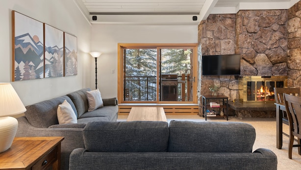 A cozy living room with a gray sofa, a wooden coffee table, and a stone fireplace.