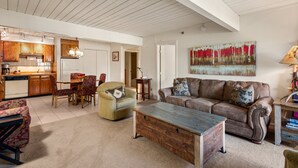 A spacious living area with a wooden ceiling, a dining table with chairs, a sofa, and a painting on the wall.