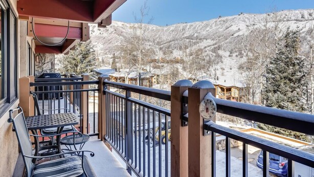 A balcony with a table and chairs, overlooking a snowy mountainous landscape.