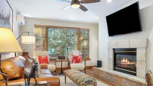 Una sala de estar con chimenea, sofá de cuero, sillones, una mesa de centro y un televisor montado en la pared.