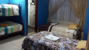 Un dormitorio con dos camas, una con una colcha estampada y la otra con una lisa. Se ve un baño a través de una puerta de vidrio.