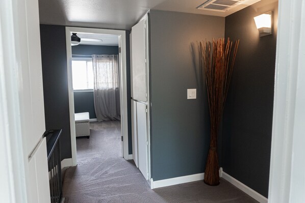 A hallway with a dark wall, a tall decorative plant, and a door leading to a room with a bed and a window with curtains. - Old Town Scottsdale hidden gem! Hot Tub is private! Inquire pricing! (Scottsdale)