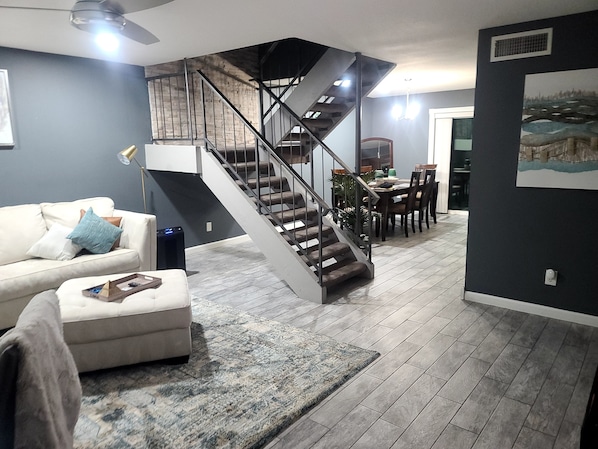 Una sala de estar moderna con una escalera, un comedor y una cocina al fondo.