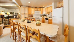 A spacious kitchen with wooden cabinets, a central island with chairs, and modern appliances. - 1BR condo Base Village with pool, hot tub, 700 Stonebridge Condos (Snowmass Village)