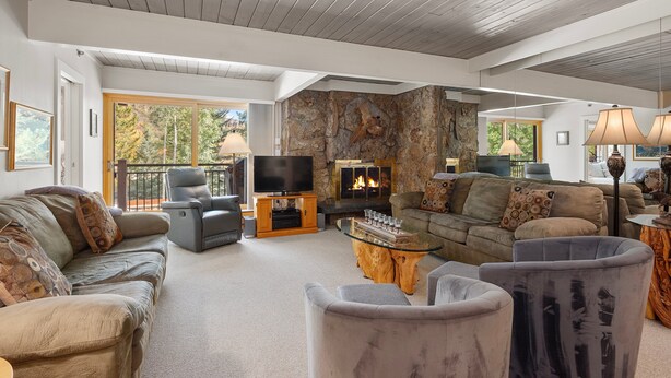 A spacious living room with a stone fireplace, comfortable seating, a flat-screen TV, and a large window offering a view of the outdoors. - 1BR condo Base Village with pool, hot tub, 700 Stonebridge Condos (Snowmass Village)