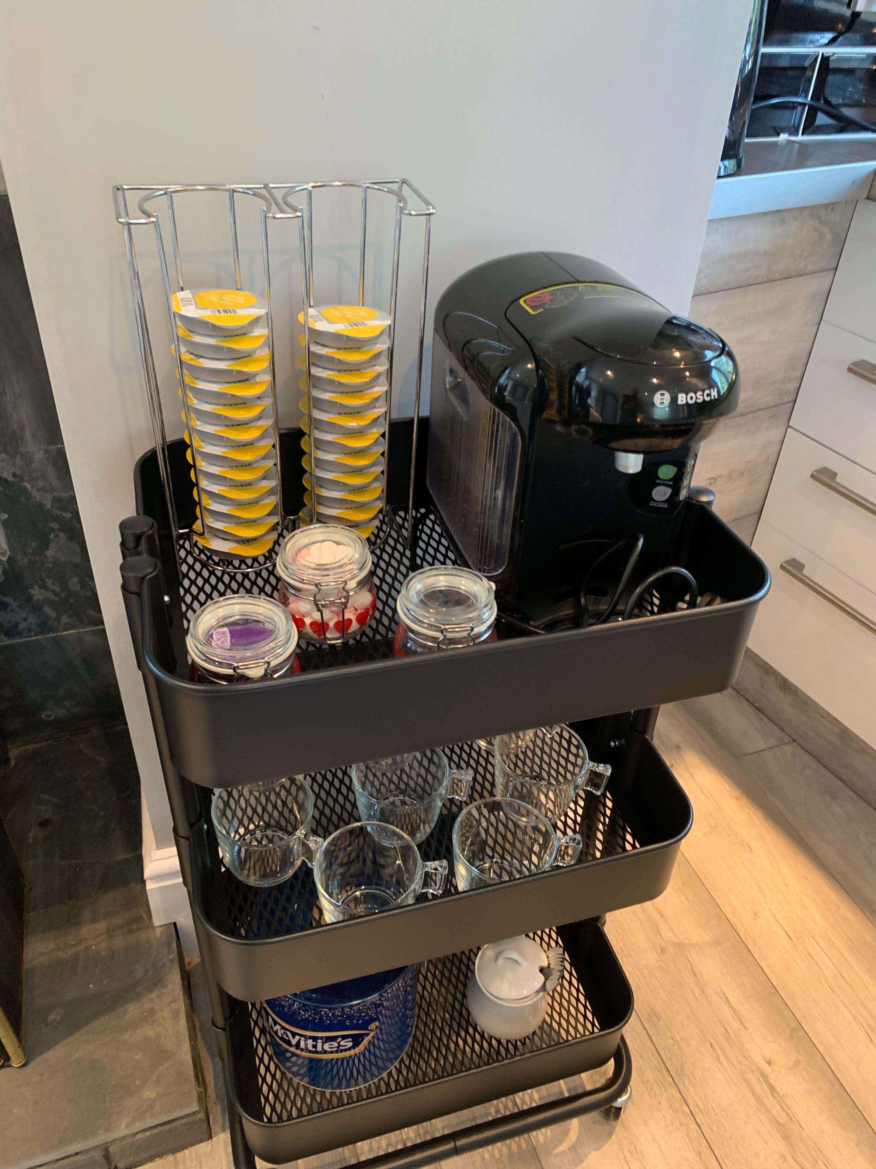 Une machine à café sur un chariot, avec plusieurs tasses à café, un pot de sucre et un récipient de crème à café.