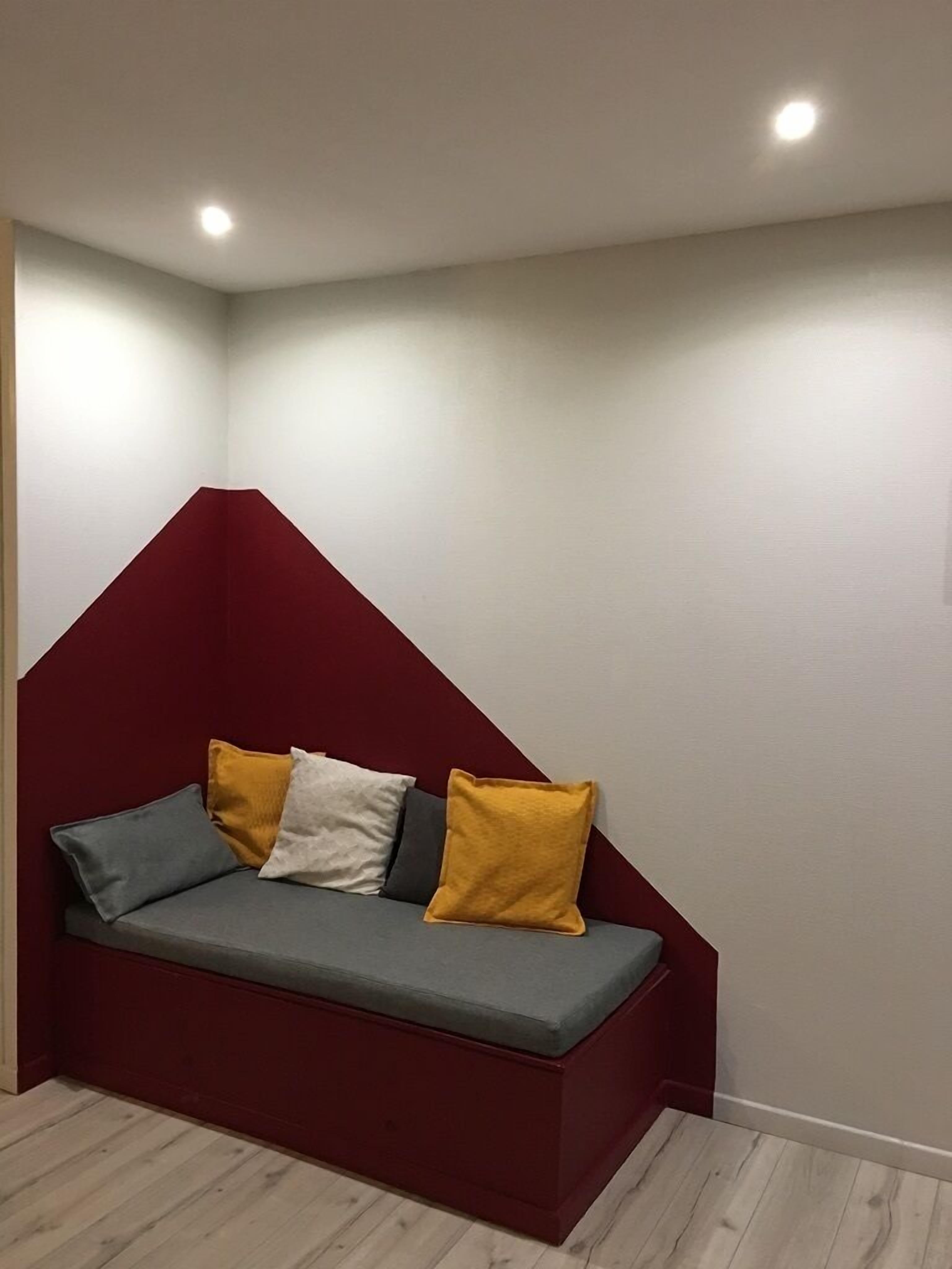 Un canapé d’angle avec un dossier rouge et des coussins jaunes et gris.