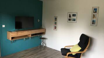 Una sala de estar con paredes color esmeralda, un mueble de madera para entretenimiento, un sofá negro con un cojín amarillo y un televisor montado en la pared.