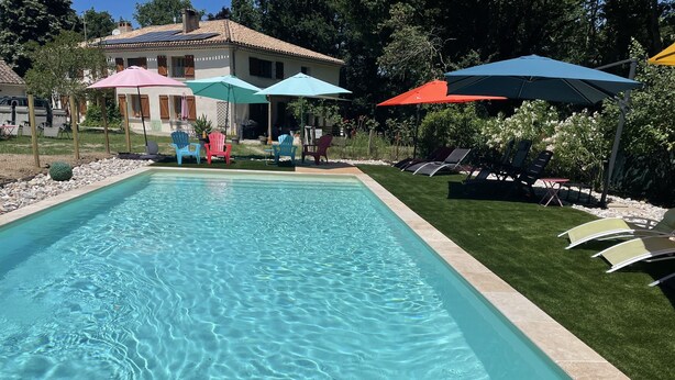 A rectangular swimming pool with clear water, surrounded by a tiled deck. There are colorful umbrellas and chairs around the pool area. - La Forestière (Monclar-de-Quercy)