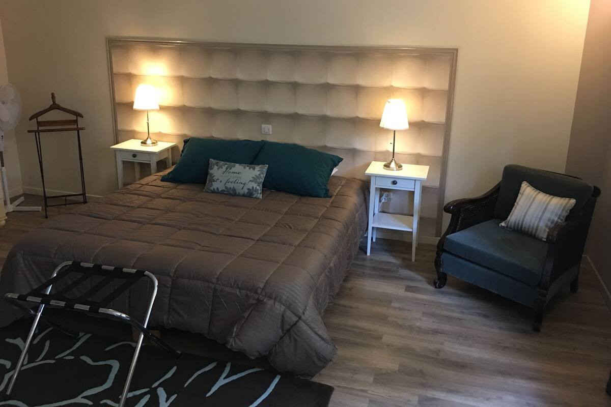 A bedroom with a large bed, two bedside tables with lamps, a chair, and a hanging rack.