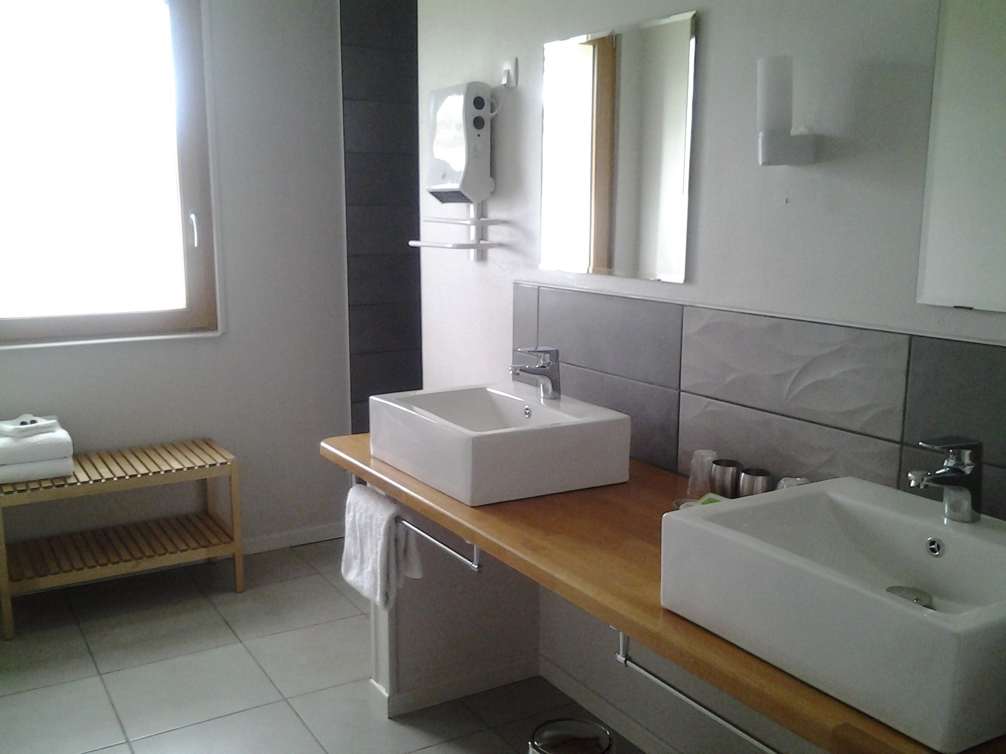 A modern bathroom with two sinks, a towel rack, and a shelf with towels.