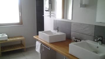A modern bathroom with two sinks, a towel rack, and a shelf with towels.