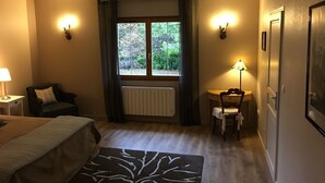 A hotel room with a bed, a desk, a chair, a window with curtains, and wall-mounted lights. - La Forestière (Monclar-de-Quercy)
