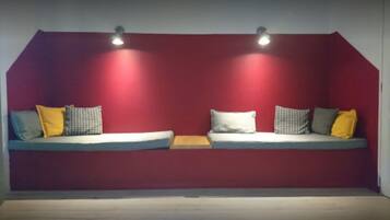 A room with a red wall, two windows, and a bench with cushions.