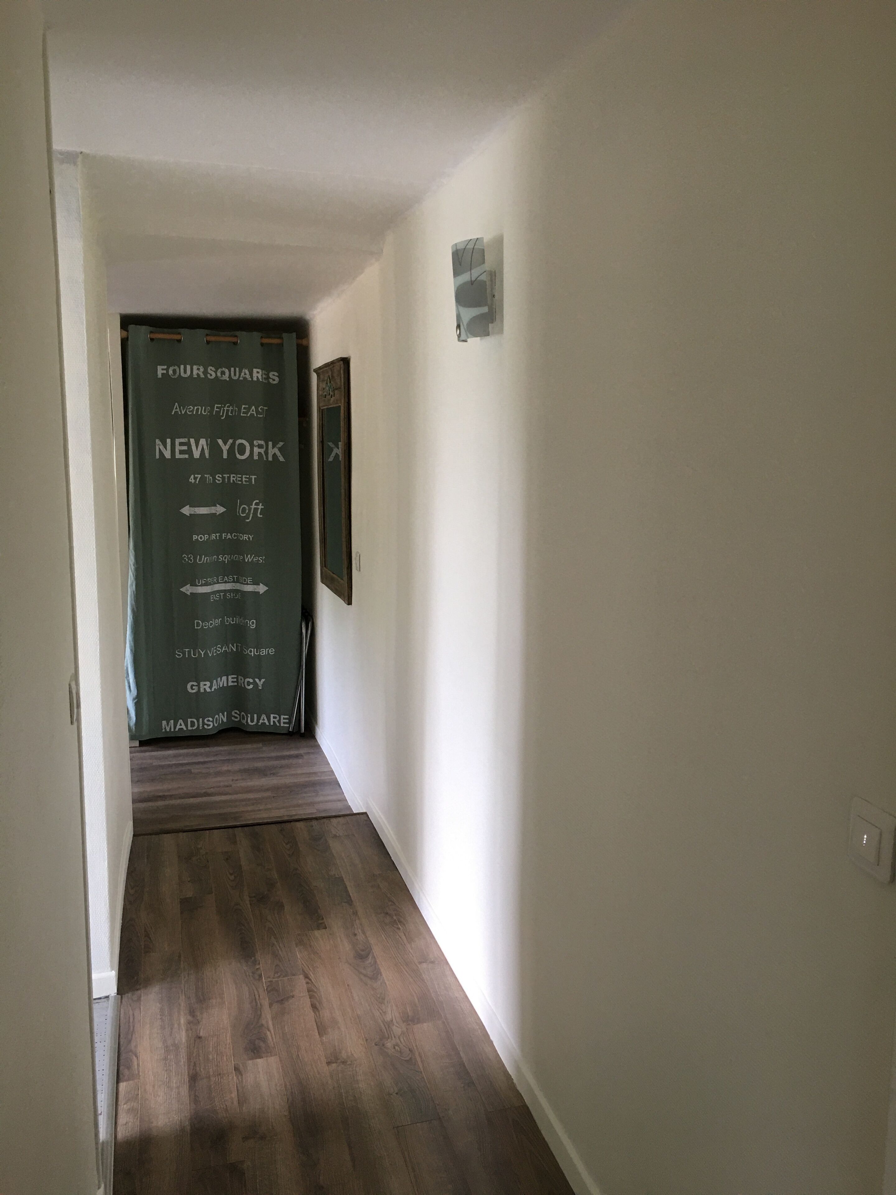 A hallway with a wooden floor and a door with a sign listing nearby locations.