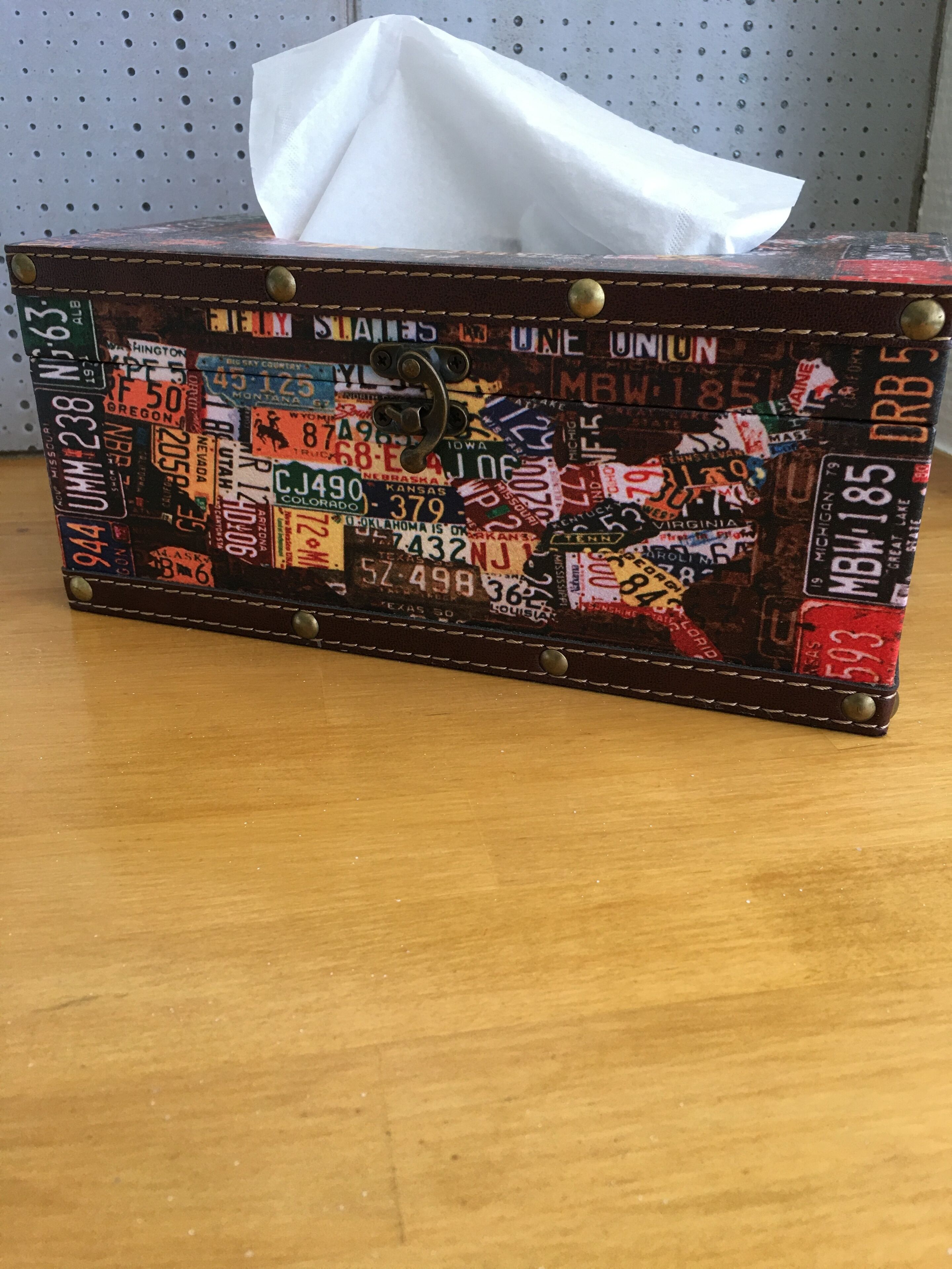 Una maleta antigua con una caja de pañuelos en su interior, decorada con diversas matrículas estatales.