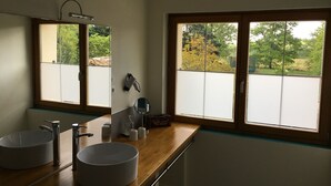A bathroom with two sinks, a mirror, and a window with a view of greenery. - La Forestière (Monclar-de-Quercy)