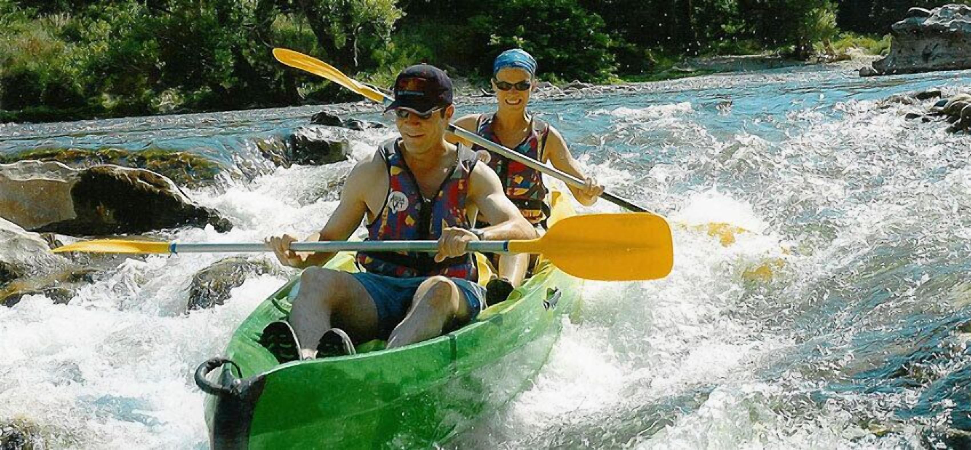 Two people kayaking on a river with rapids.