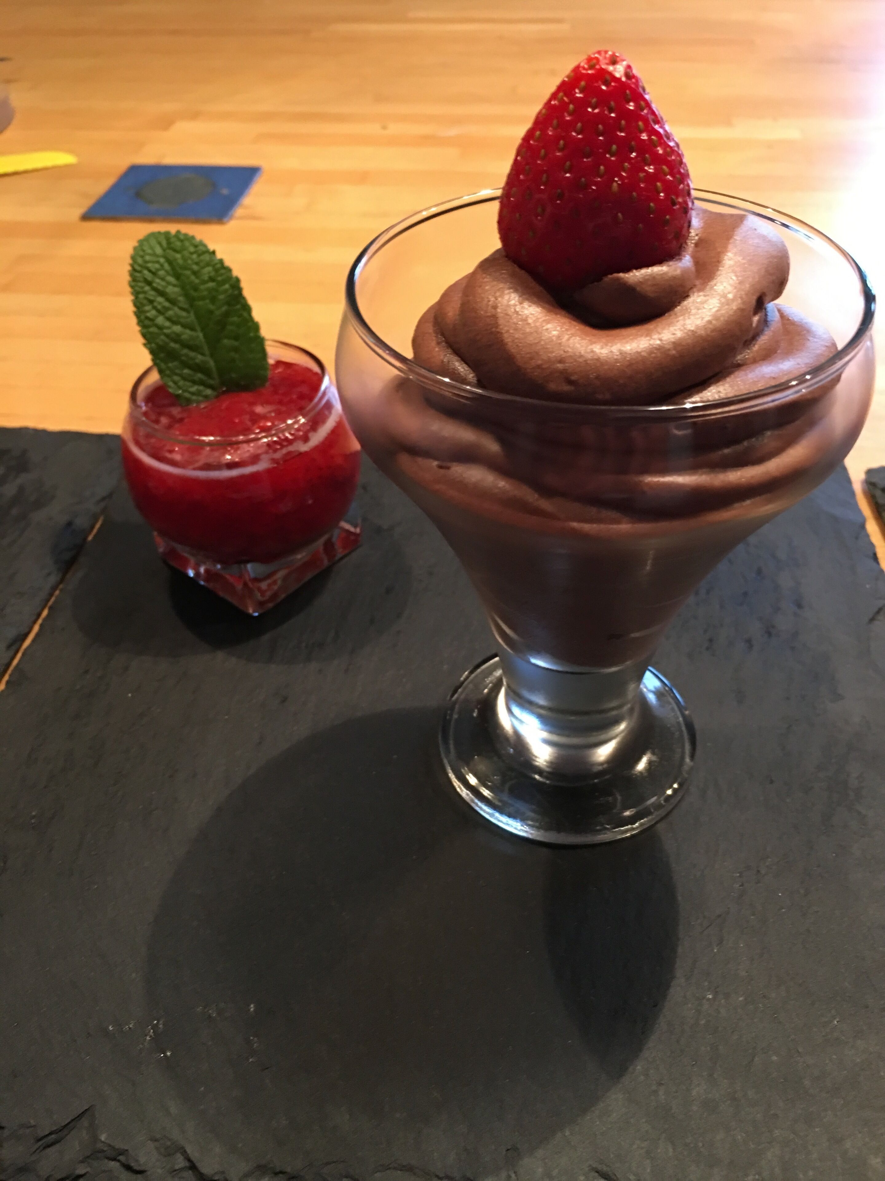 Un dessert con una fragola sopra, su una superficie di ardesia scura.