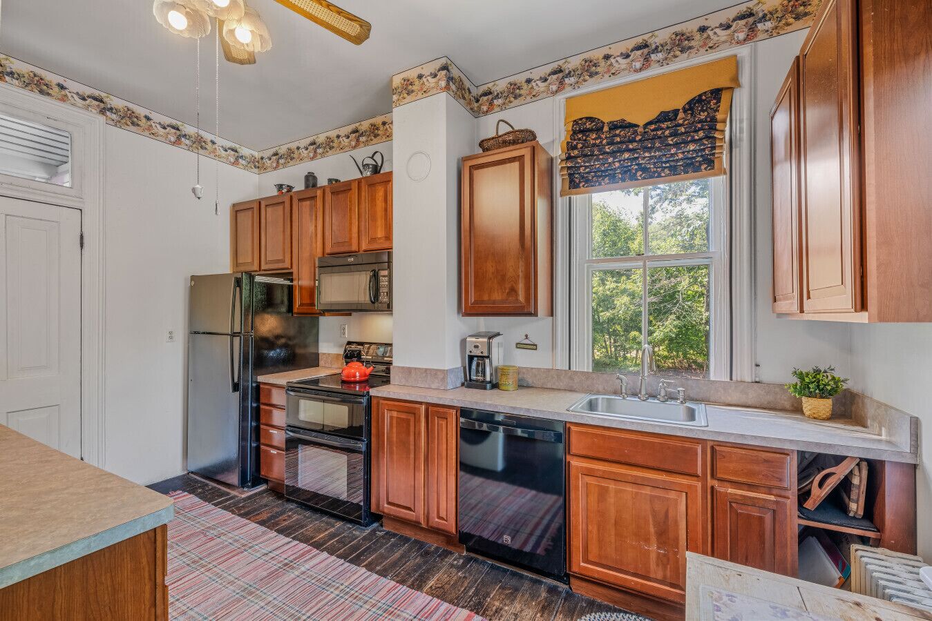 Una cocina con armarios de madera, refrigerador, estufa, microondas y ventana con vista a la vegetación.