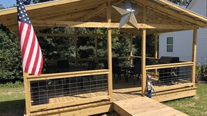 Une terrasse en bois avec un espace couvert, un barbecue et un drapeau américain.