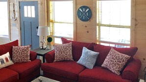 L’intérieur d’un chalet accueillant, avec un canapé rouge, une petite table et une horloge murale.