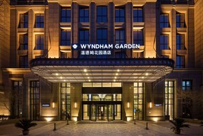 The exterior of the Wyndham Garden hotel with a prominent entrance, large windows, and a well-lit facade.