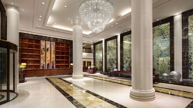 A spacious lobby with marble flooring, large columns, a grand chandelier, and a well-stocked reception area.