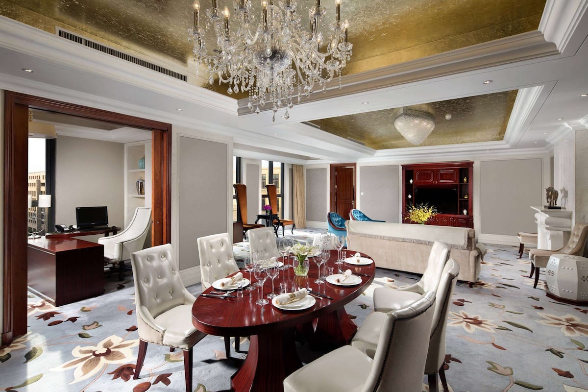 A spacious dining area with a large round table, elegant chairs, and a chandelier.