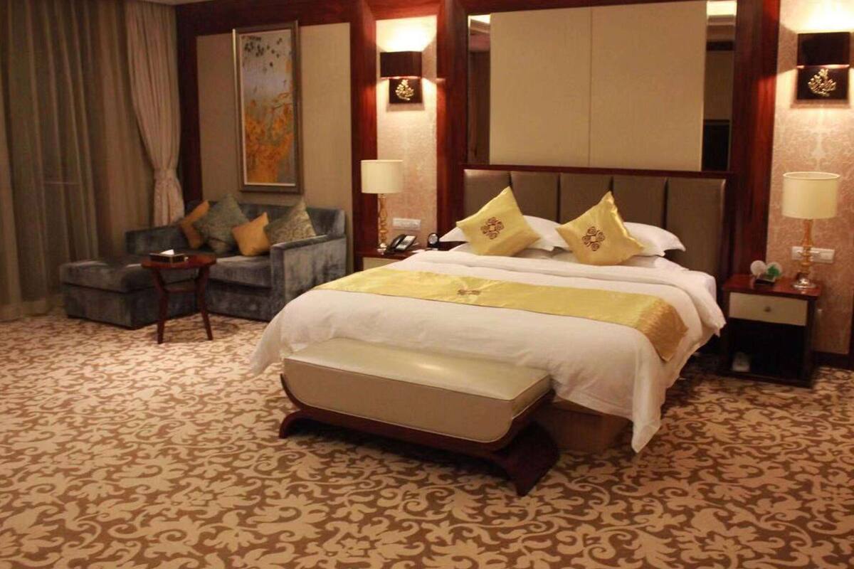 A hotel room with a large bed, a sofa, a desk, and a mirror.