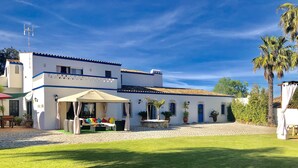 A white building with blue trim, a covered seating area with colorful cushions, and a cobblestone courtyard. - Beautiful Restored Algarve Typical Farmhouse, With Private Pool And Sea Views (Loulé)