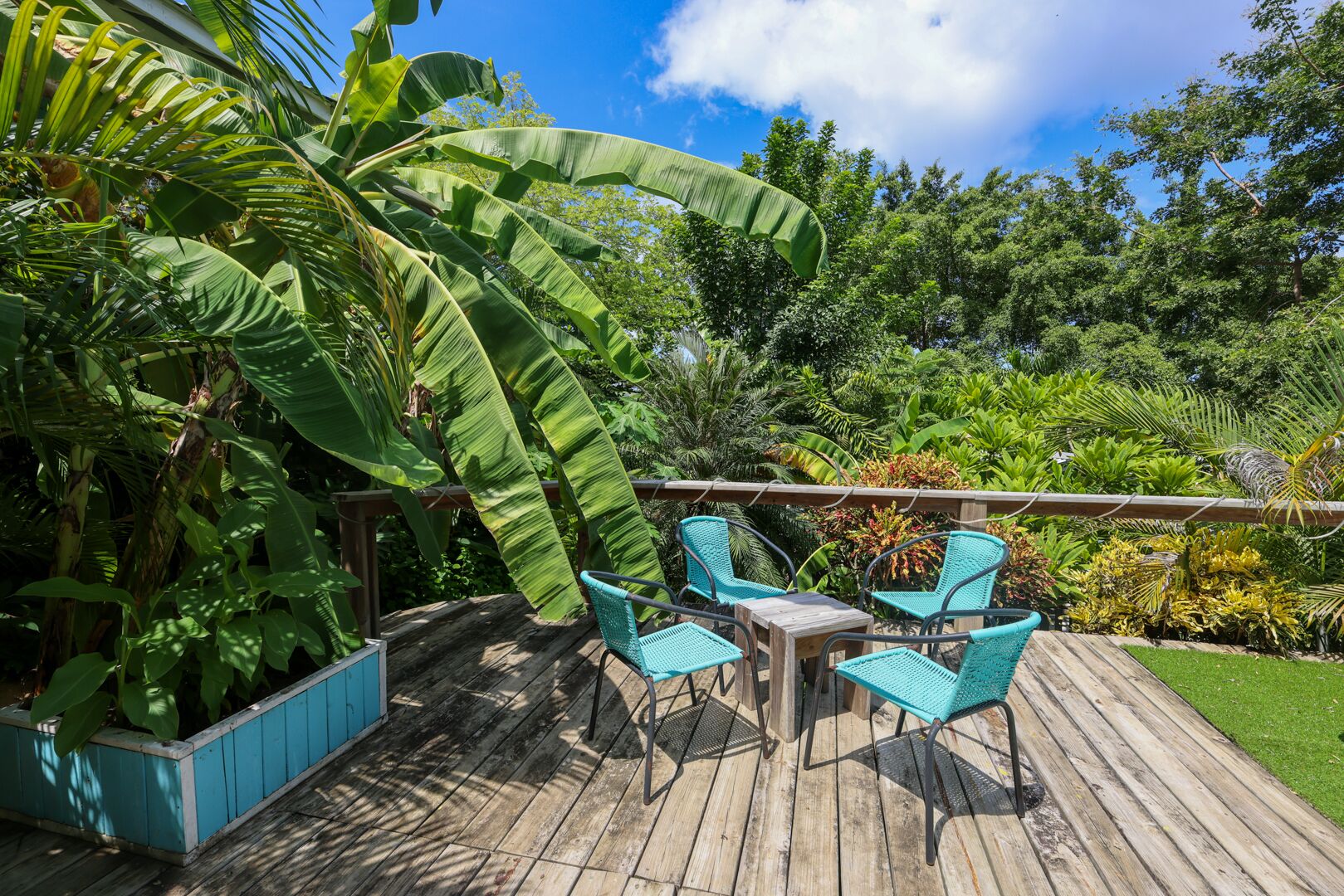 A wooden deck with outdoor furniture, surrounded by lush tropical plants and trees.