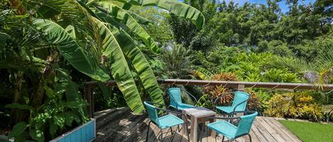 Una terraza de madera con mobiliario exterior, rodeada de exuberante vegetación tropical y árboles.