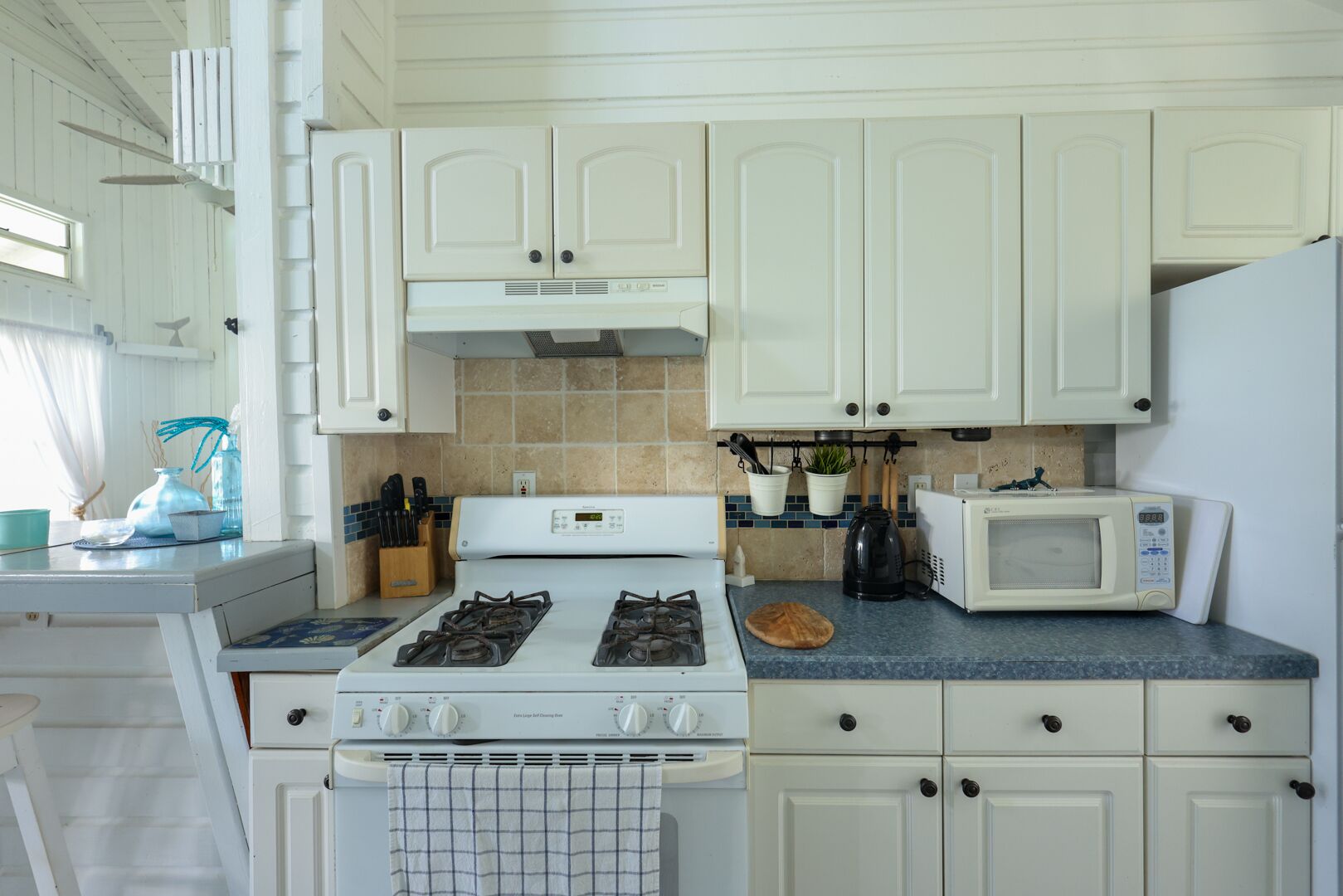 A kitchen with white cabinets, a stove, a microwave, and a sink.