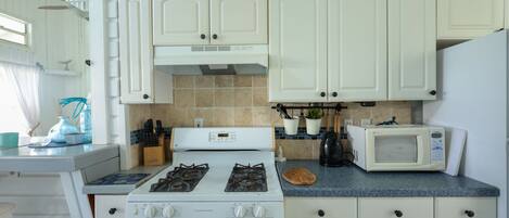 A kitchen with white cabinets, a stove, a microwave, and a sink.