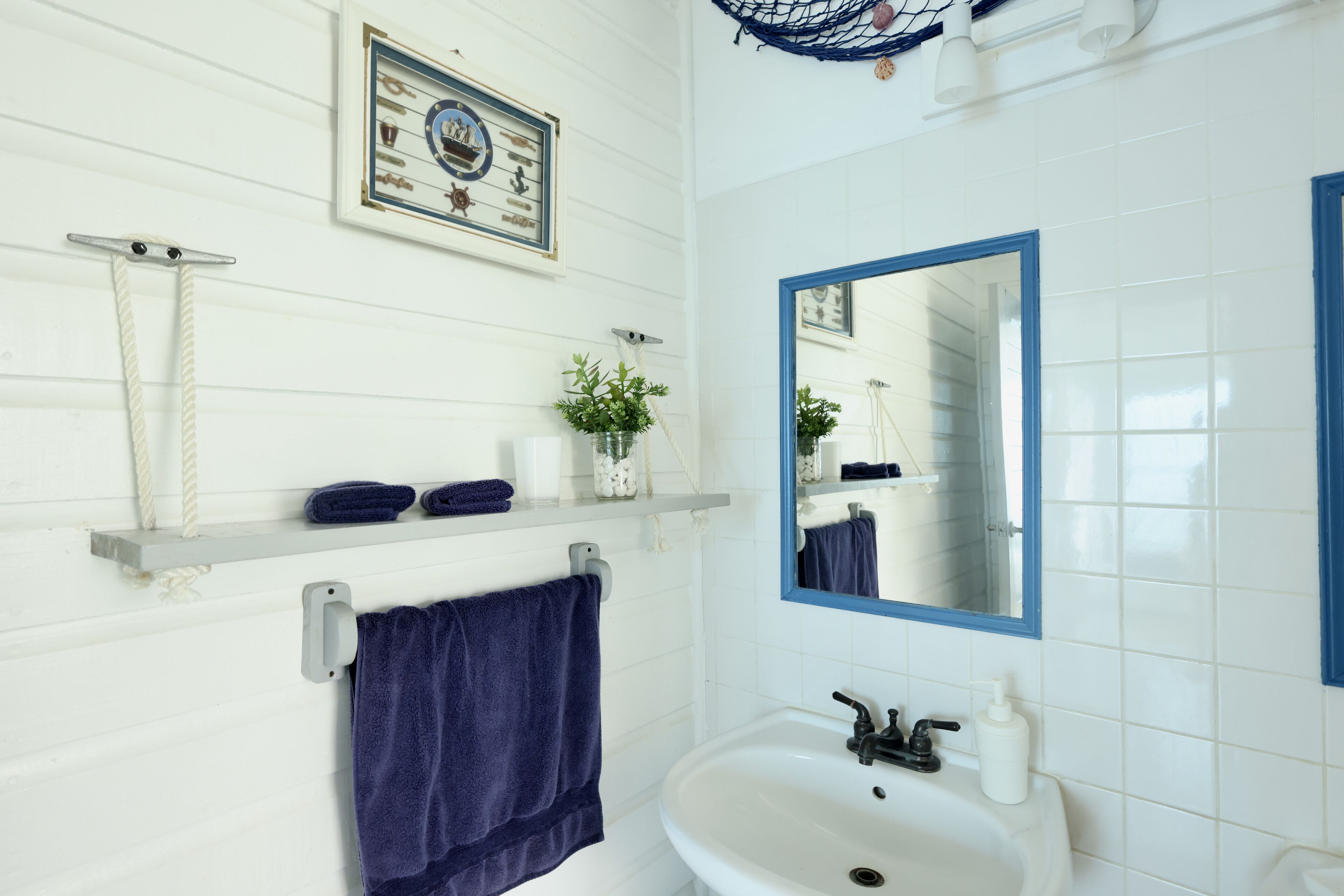 A bathroom with a white sink, a blue-framed mirror, a towel rack with a blue towel, and a shelf with toiletries.