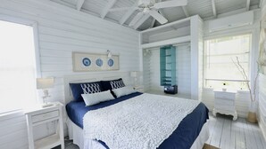 A bedroom with a bed, white walls, a ceiling fan, and a window with blinds.