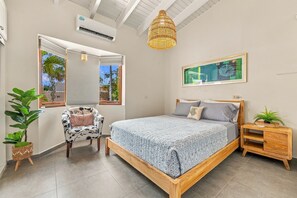 Una camera da letto con un letto, una sedia, un comodino, un lampadario e un condizionatore d'aria a parete, oltre a una finestra con vista.
